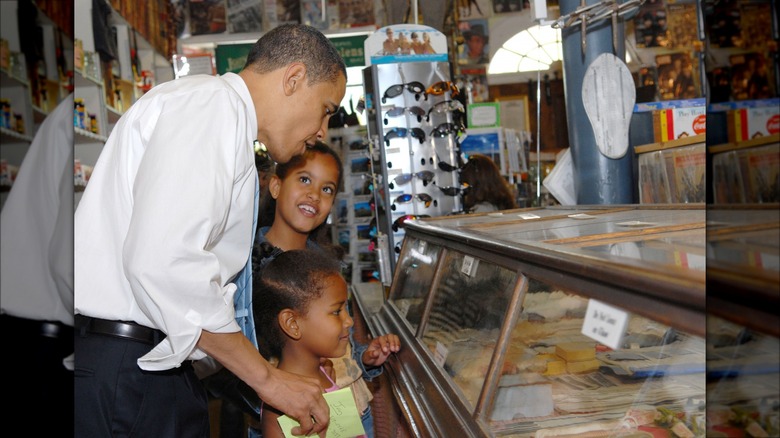 Malia and Sasha Obama smiling with Barack Obama at a general store