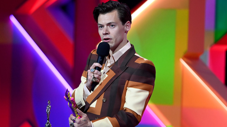 Harry Styles, wearing a patterned Gucci suit, accepting a Brit Award, speaking into the microphone