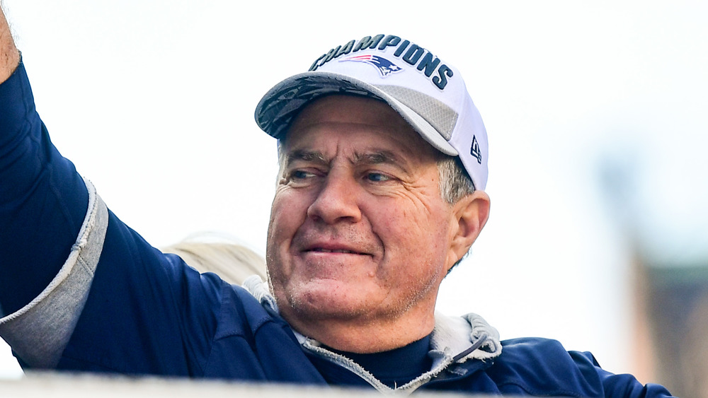 Bill Belichick looks to his right smiling and wearing a cap reading "Champions"