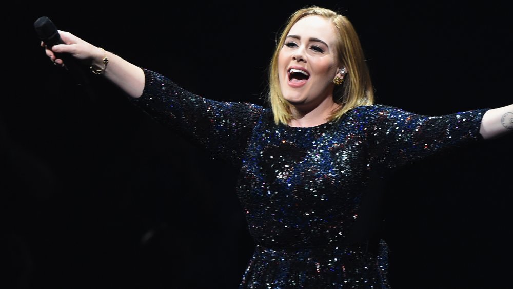 Adele smiling onstage and pointing the mic toward her audience