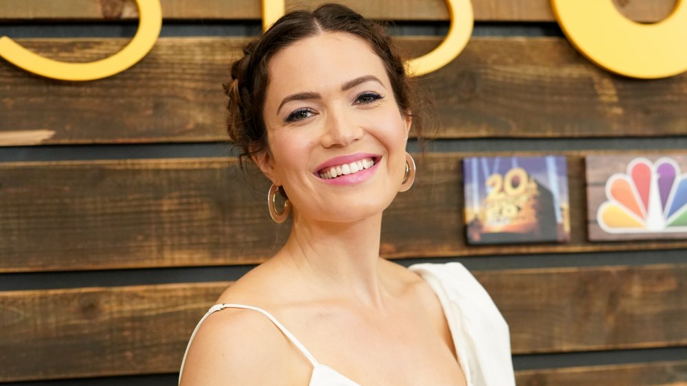 Mandy Moore in a white outfit, smiling with her hair pulled back at a This Is Us-themed event