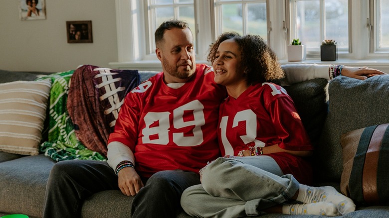 Dad and daughter smiling, watching football