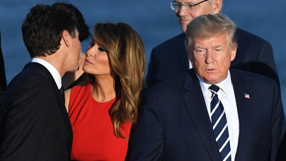 Melania Trump and Justin Trudeau greeting one another with a peck, Donald Trump to the side