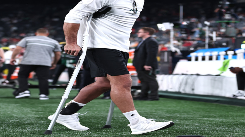 Aaron Rodgers using crutches wearing a white long-sleeved t-shirt