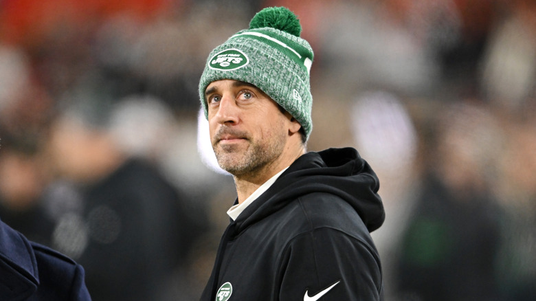 Aaron Rodgers looking upward wearing a black hoodie and green beanie