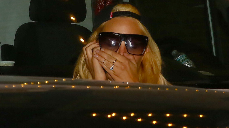 Amanda Bynes in ball cap and sunglasses, covering mouth