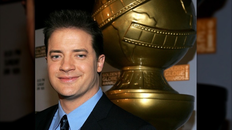 Brendan Fraser smiling in front of Golden Globe statue