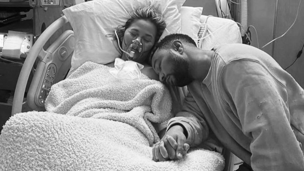 Chrissy Teigen and John Legend holding hands and resting in her hospital room