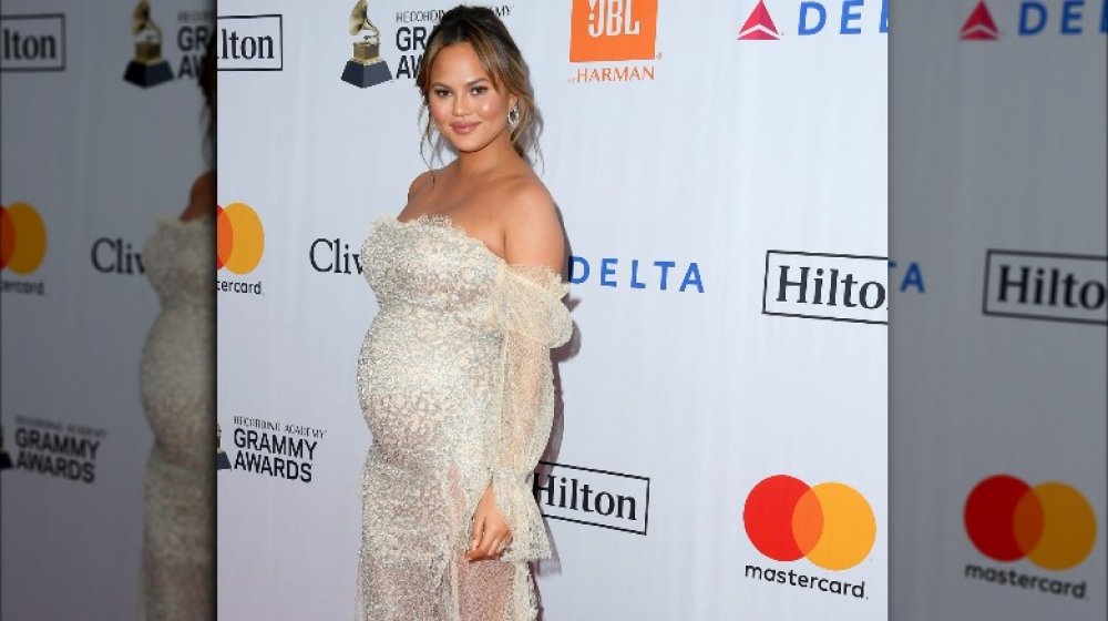 Chrissy Teigen posing from the side and smiling, showing off her baby bump