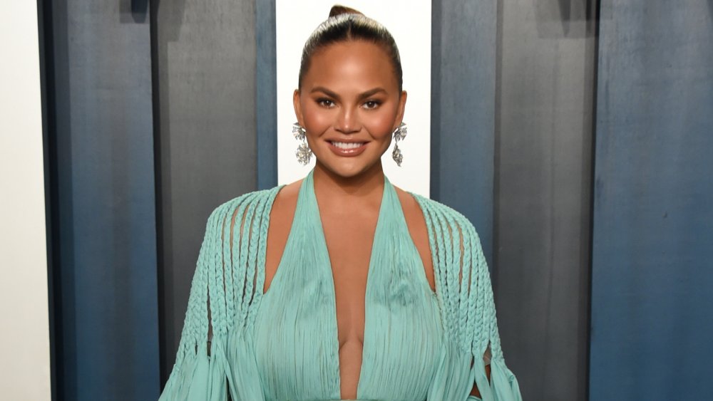 Chrissy Teigen smiling while posing in a light blue dress at the 2020 Vanity Fair Oscar Party