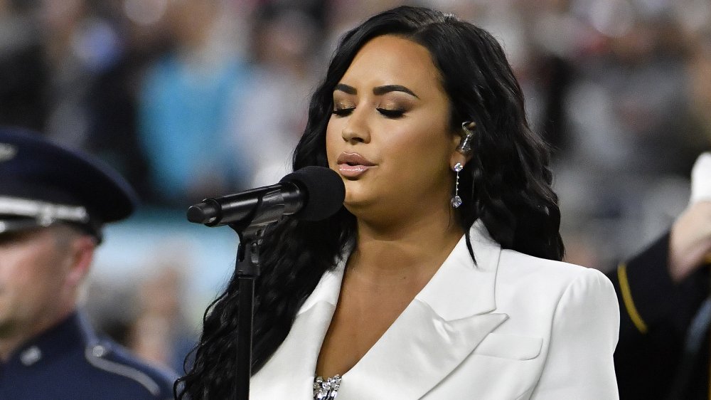 Demi Lovato on stage, singing in a white blazer