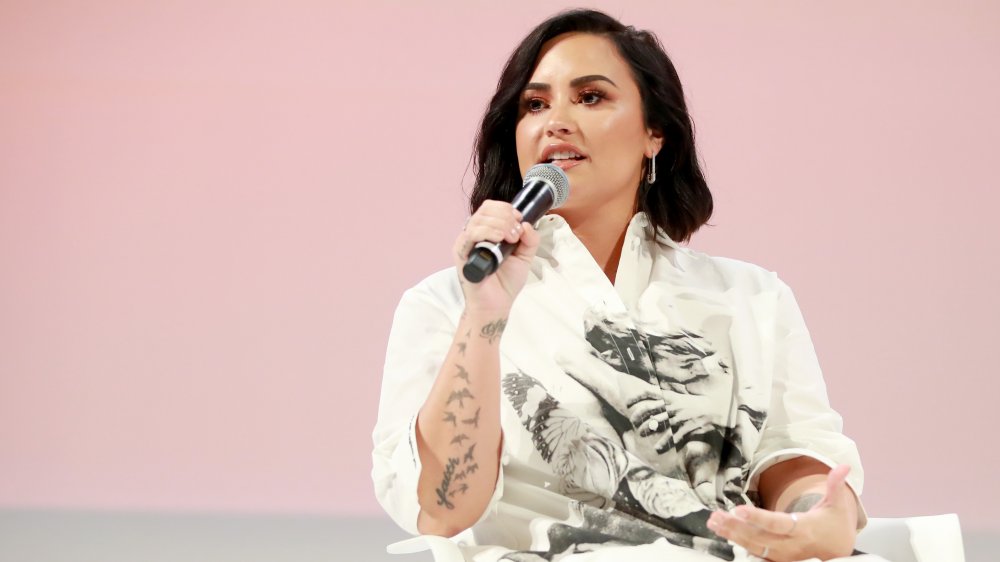 Demi Lovato at a panel, microphone in hand, speaking