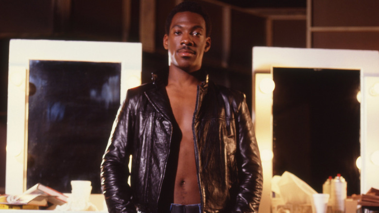 Eddie Murphy posing shirtless wearing a leather jacket