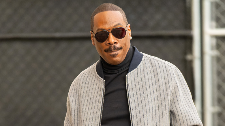 Eddie Murphy wearing sunglasses, a black turtleneck, and a grey pinstriped jacket