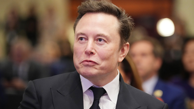 Elon Musk wearing a suit with frowning lips