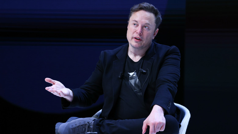 Elon Musk sitting ina chair with his arm out