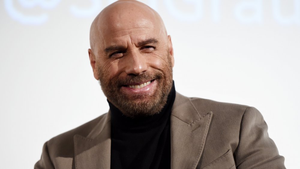 John Travolta, bald, smiling in grey suit