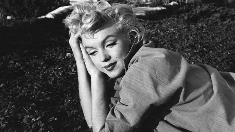 Marilyn Monroe lying down outside while propped on her elbows 