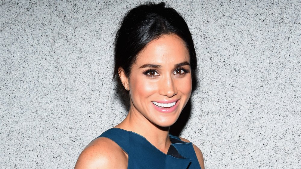 Meghan Markle in a blue dress, smiling at camera