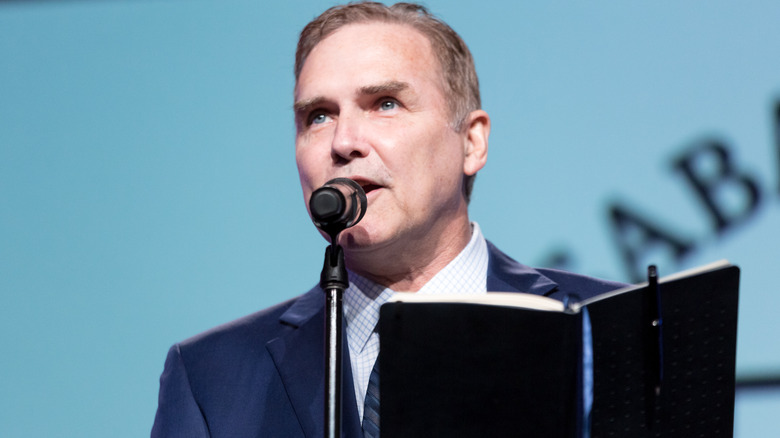 Norm Macdonald holding a book while speaking