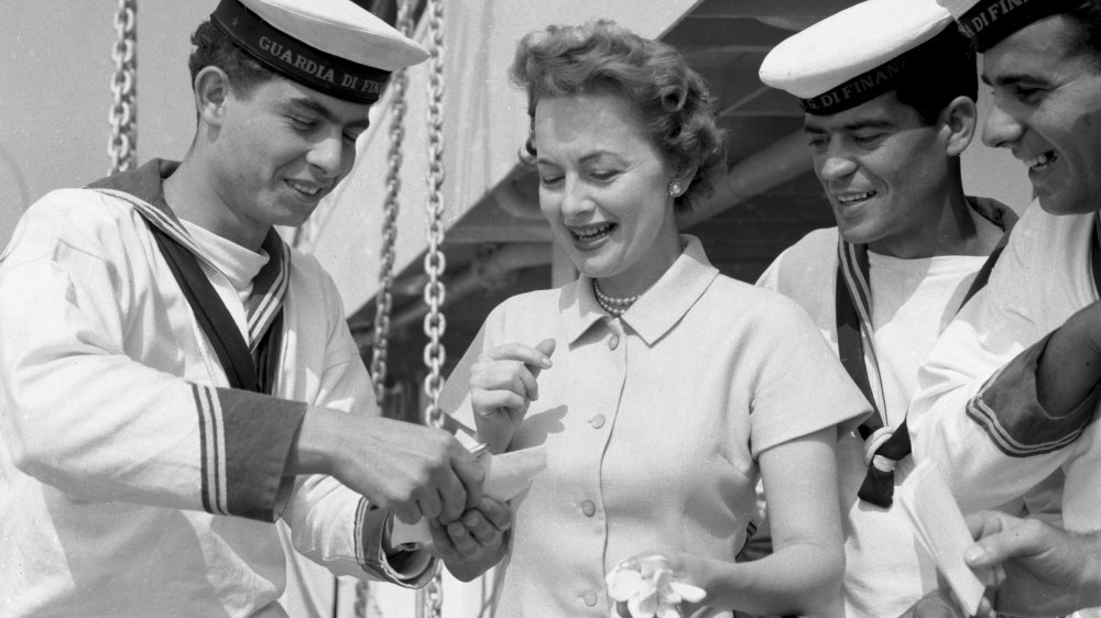 Black-and-white photo of Olivia de Havilland smiling, surrounded by sailors in 1953