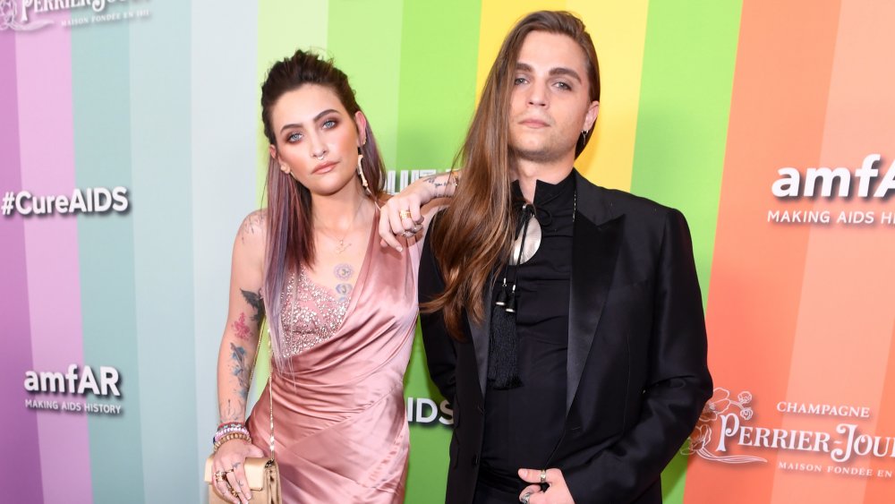 Paris Jackson y Gabriel Glenn posando juntos frente al muro de #Cure AIDS