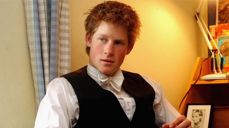 Prince Harry wearing a black vest and white bow tie while sitting in a chair