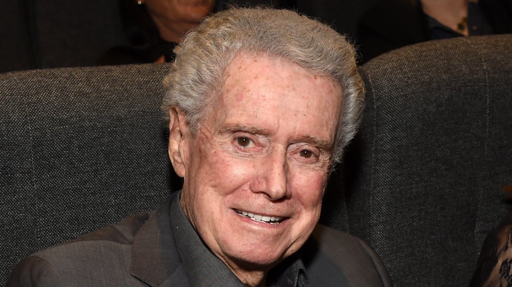 Regis Philbin in a grey suit, sitting at an event with a small smile