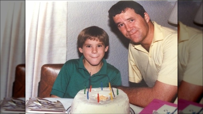 A young Ryan Reynolds smiling with his father in front of a birthday cake