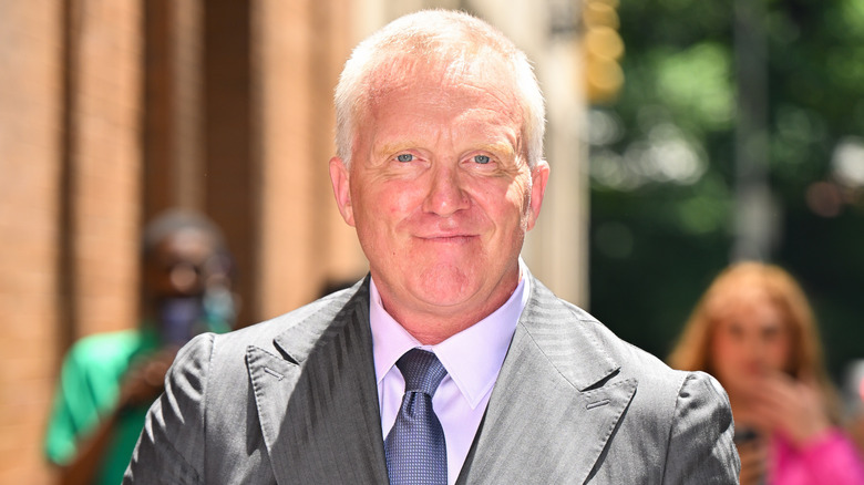 Anthony Michael Hall wearing a grey suit and smiling in the street