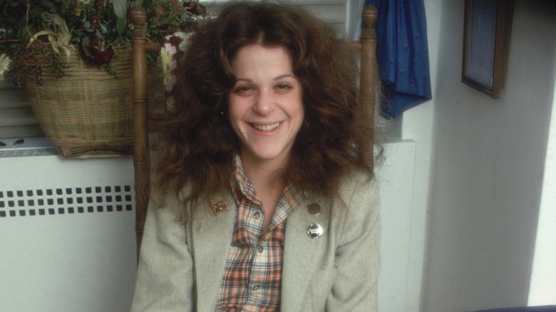 Gilda Radner sitting in a chair and smiling for a photographer