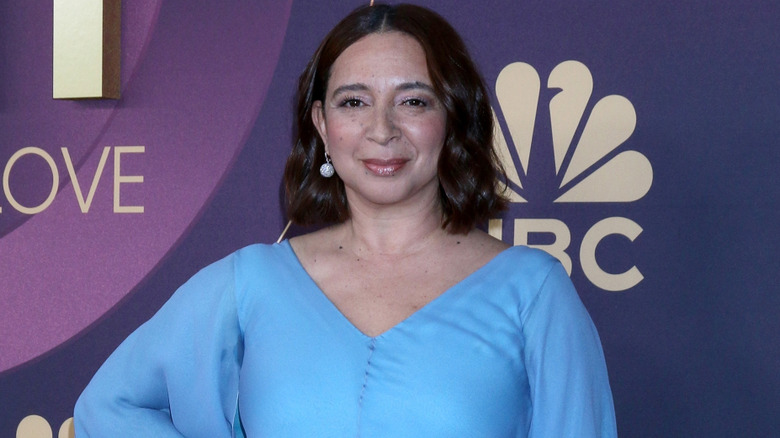 Maya Rudolph smiling and posing for photographers at an event while wearing a blue dress