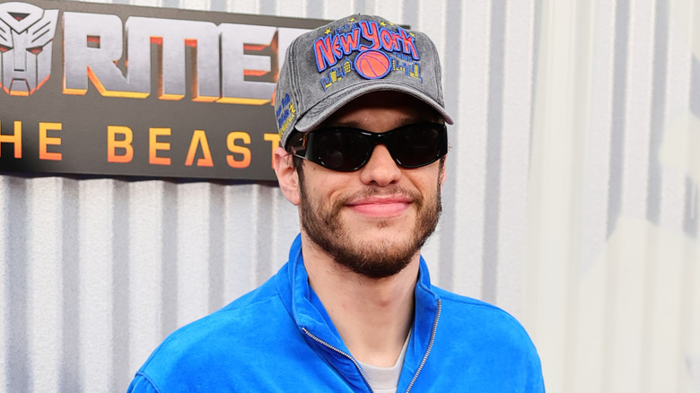 Pete Davidson smiling and wearing a blue Transformers outfit at a premiere