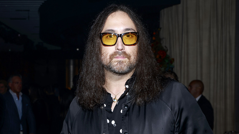 Sean Ono Lennon wearing a black jacket, white polkadot shirt, and yellow-tinted glasses