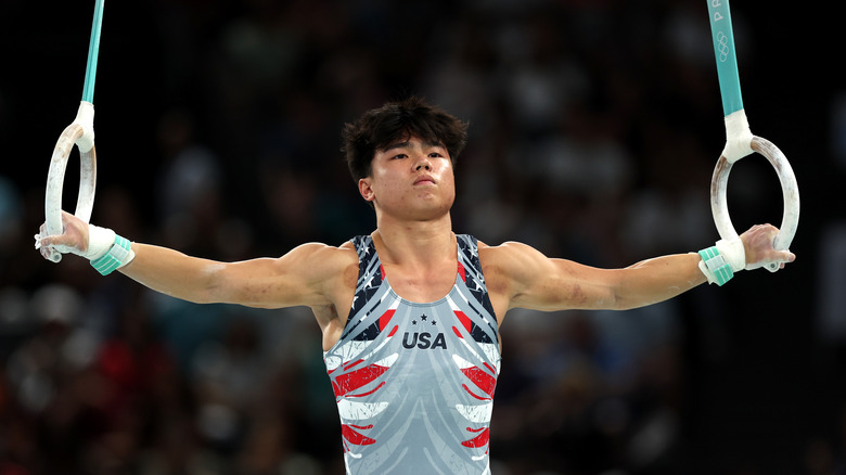 Asher Hong holding gymnastics rings while wearing a grey USA-adorned tank top