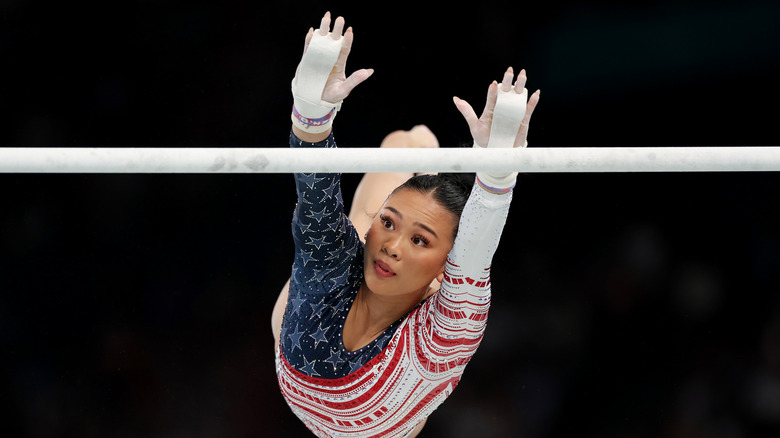 Suni Lee performing a gymnastics stunt wearing a red, white and blue bedazzled unitard and white hand tape