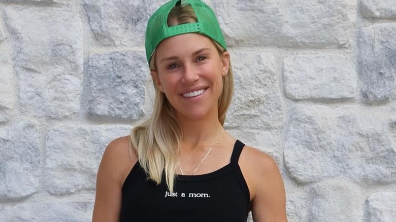 Kelly Stafford smiling wearing a backwards green snapback cap and a shirt that says 