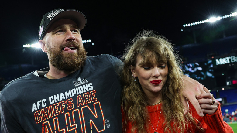 Travis Kelce stands with arm around Taylor Swift on football field