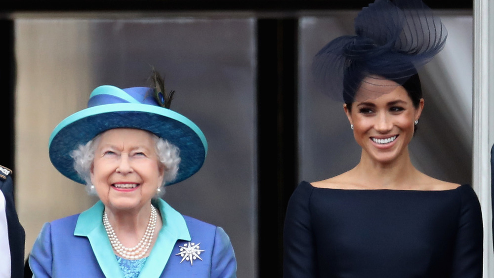 Queen Elizabeth II and Meghan Markle stand next to each other and smile 