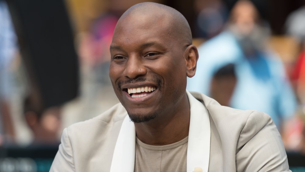 Tyrese Gibson wearing a beige blazer and shirt, smiling big at an event