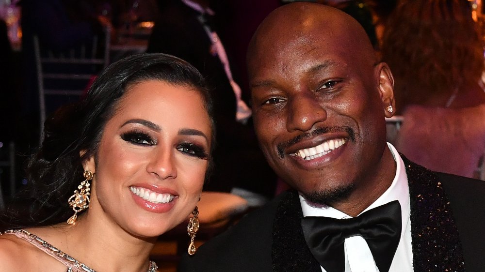 Samantha Lee Gibson in a bejeweled dress, Tyrese Gibson in a black, sparkly suit, both smiling and leaning into one another