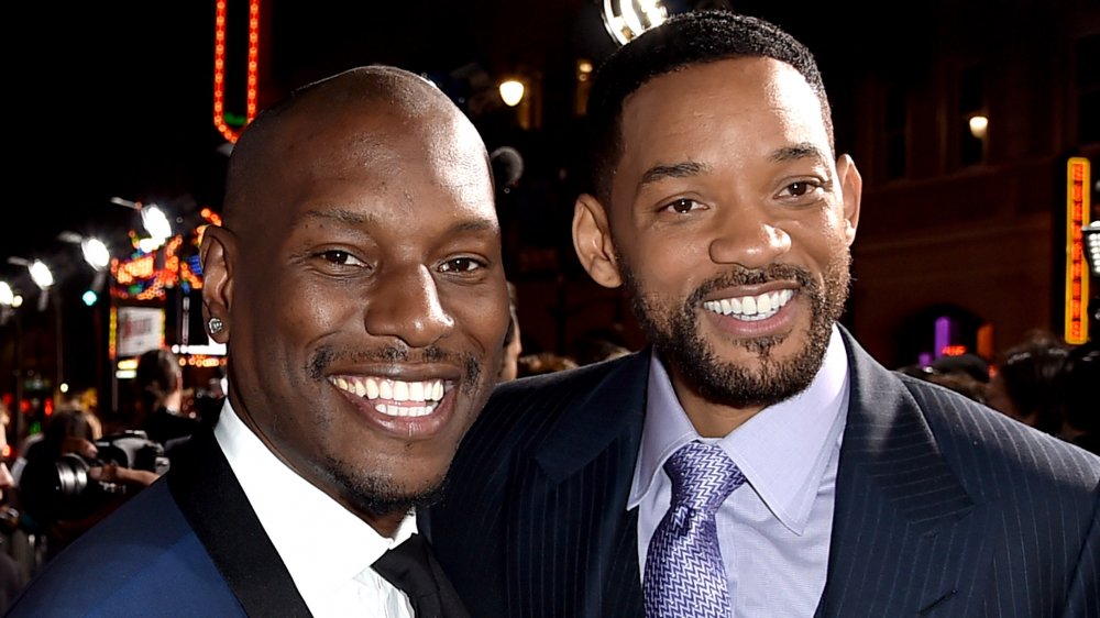 Tyrese Gibson and Will Smith, both in blue suits and smiling at an event with their arms around each other