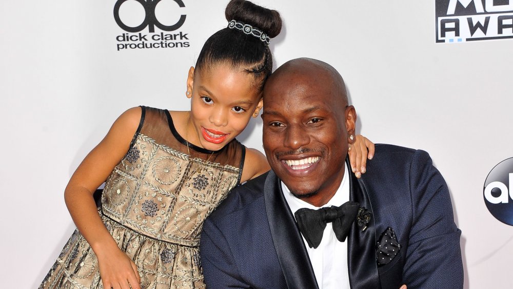 Tyrese Gibson in a blue suit, smiling and kneeling on the red carpet next to daughter Shayla Gibson