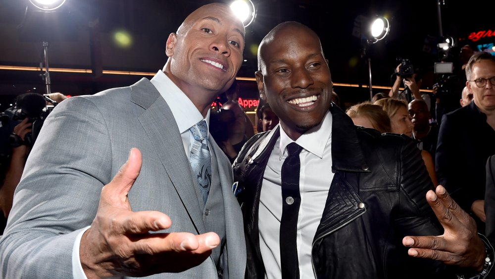 Dwayne Johnson in a grey three-piece suit, Tyrese Gibson in a black leather jacket, smiling together at a movie premiere