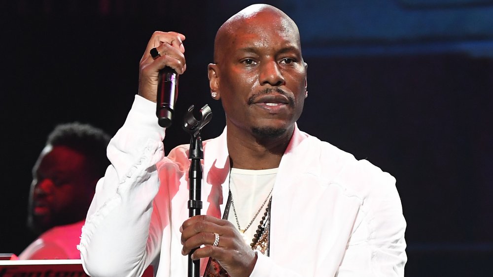 Tyrese Gibson in an all-white outfit, looking out into the audience during a live performance with a serious expression