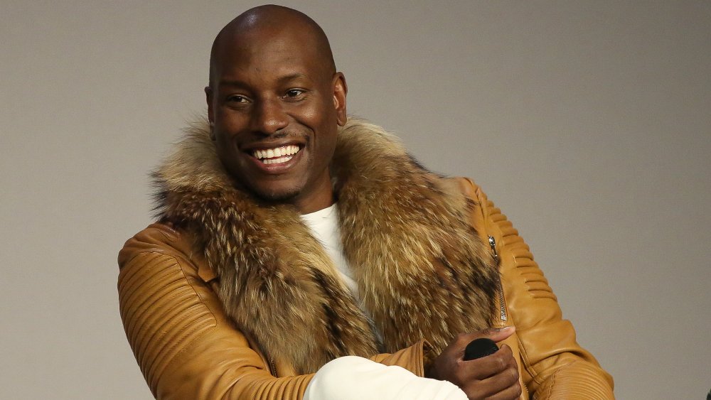 Tyrese Gibson smiling big, wearing a light brown leather jacket during an interview