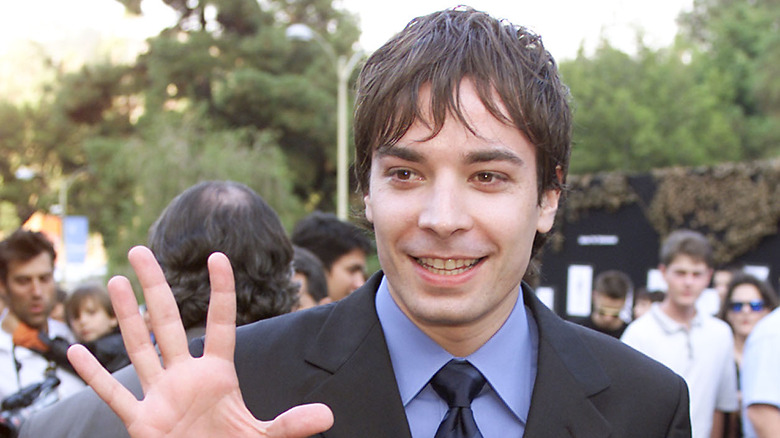 Jimmy Fallon holding his hand up and smiling