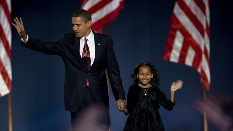 Barack Obama stands with young daughter Sasha in front of flags