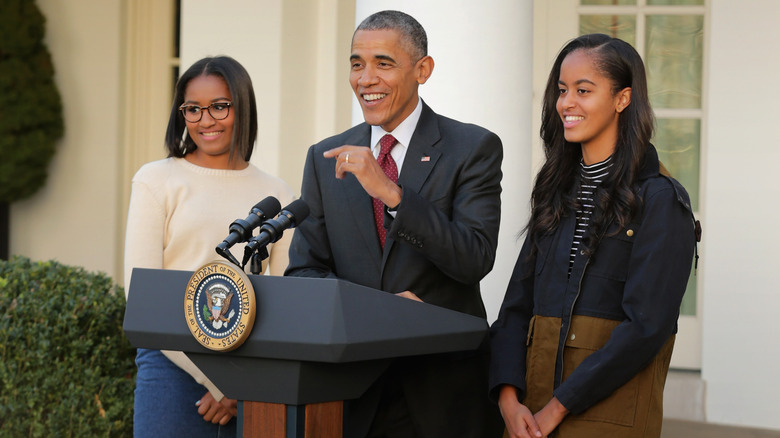 Sasha Obama, Barack Obama, and Malia Obama stand at podium