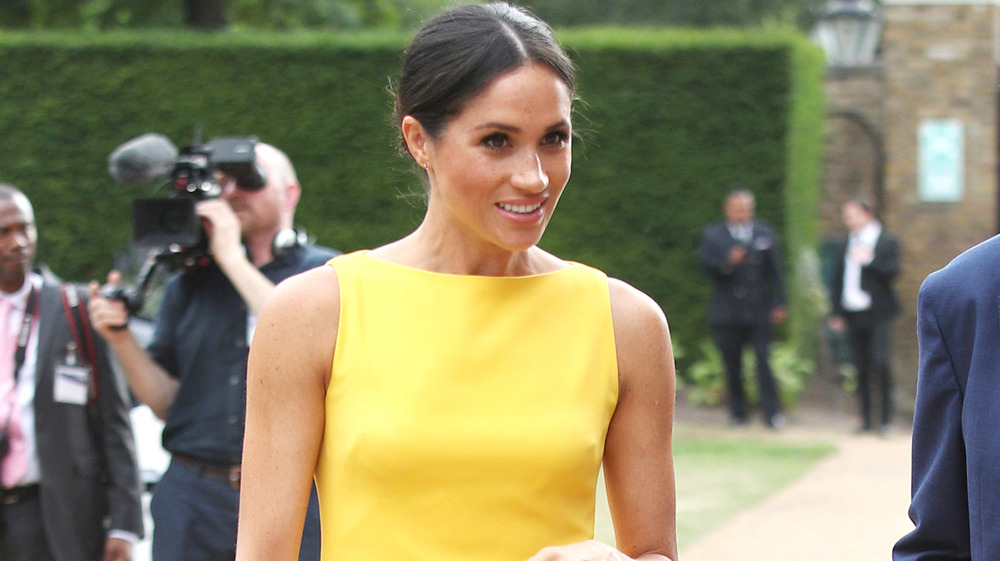 Meghan Markle walking while wearing a yellow dress